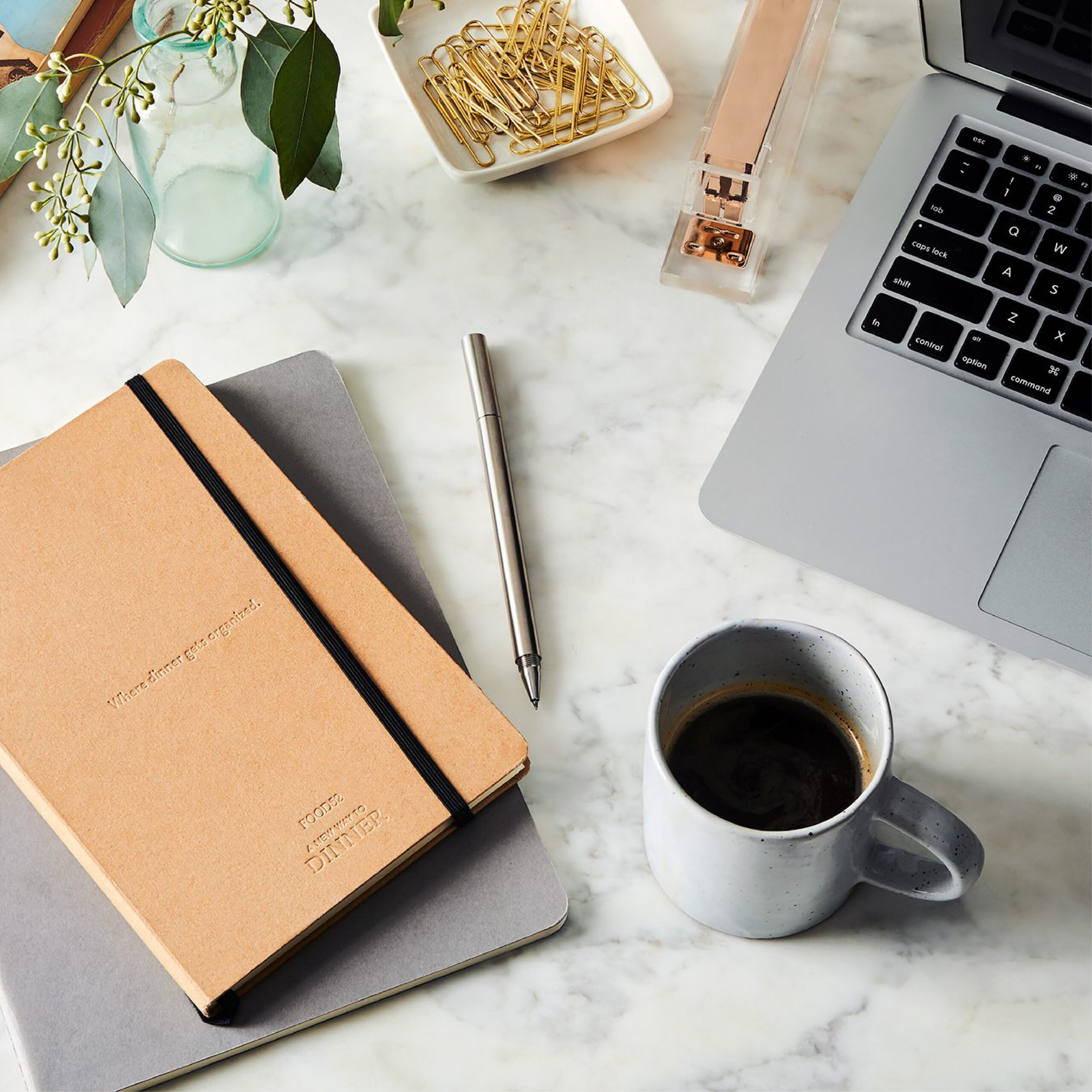 A laptop, journal, cup of coffee and other office supplies laid out on a marble table.