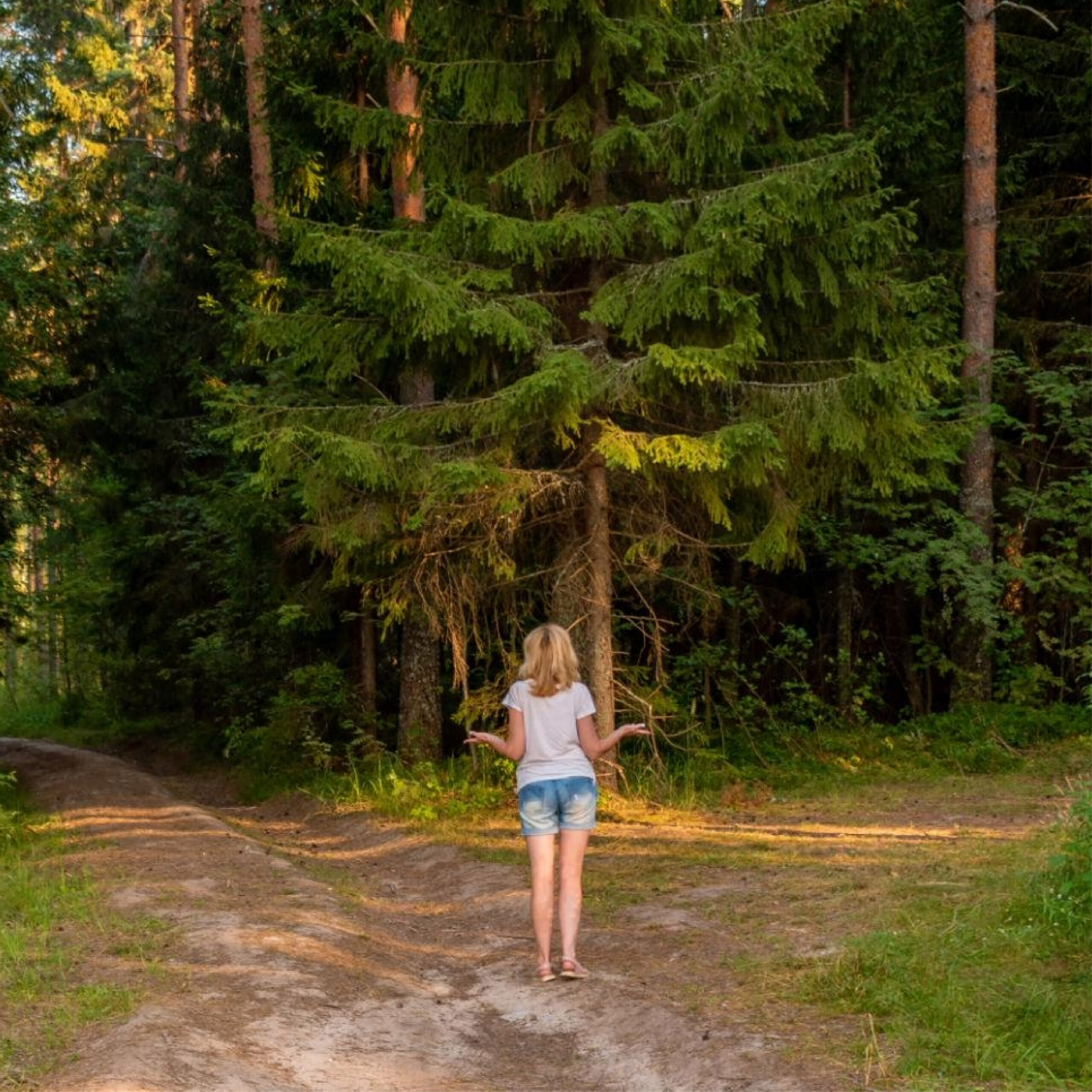 Woman standing at a fork in a wooded trail.