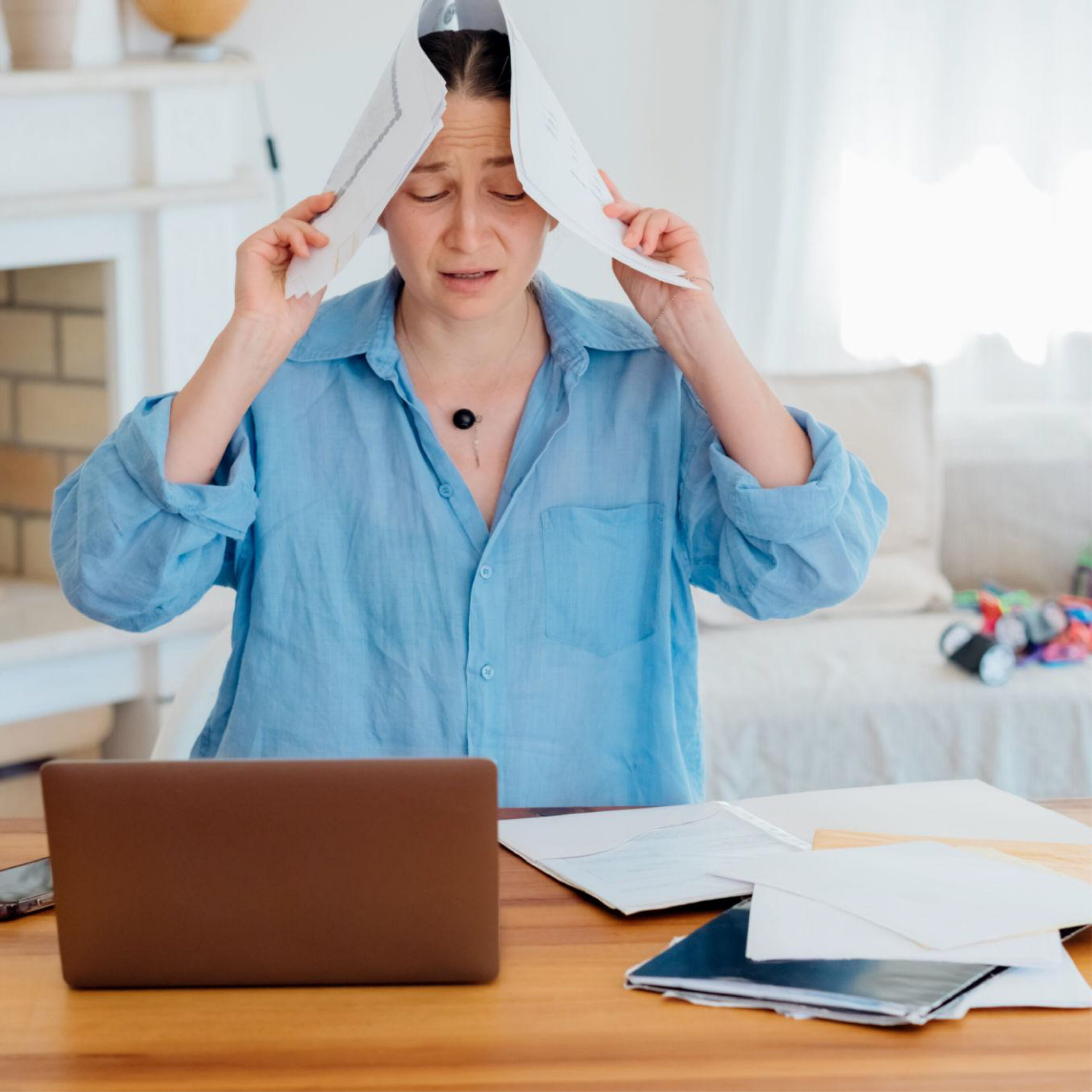 Image of a stressed woman with a laptop holding papers over her head in frustration.