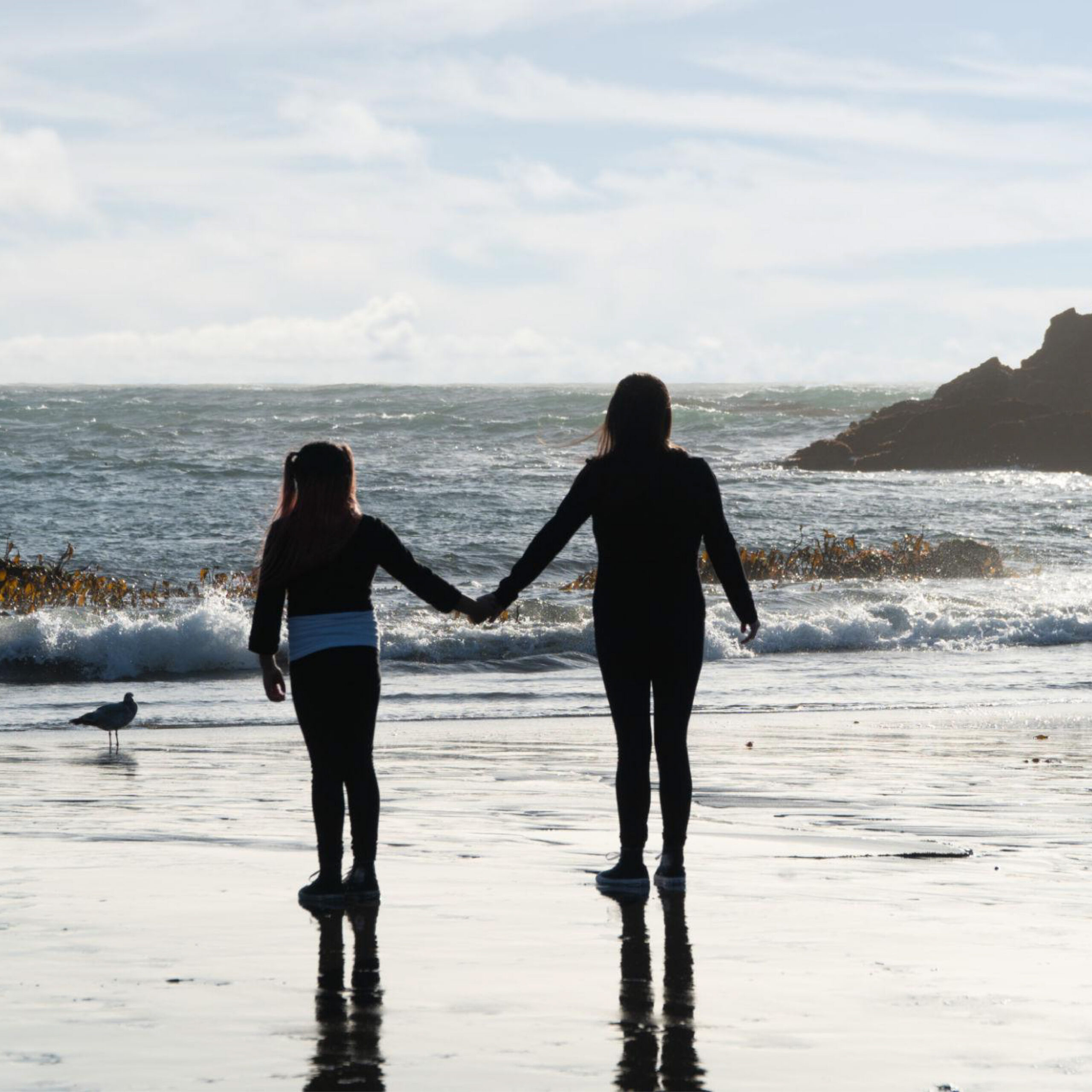 A parent and child standing on the sea shore holding hands